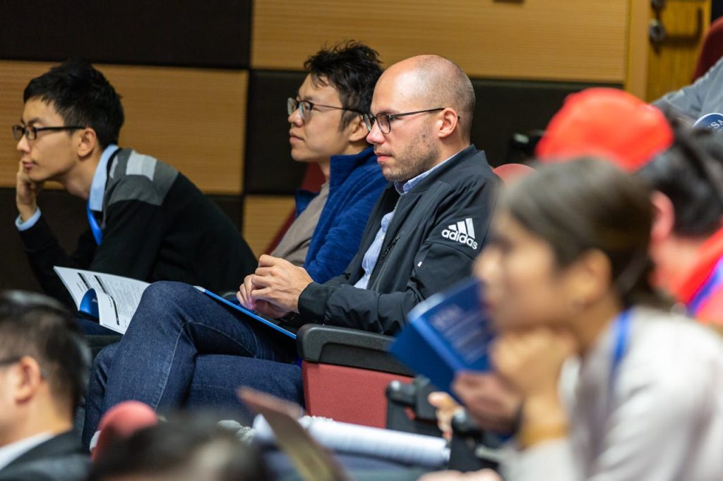 pexels photo 1708988 A diverse group of adults attentively listening to a lecture in an indoor conference setting.