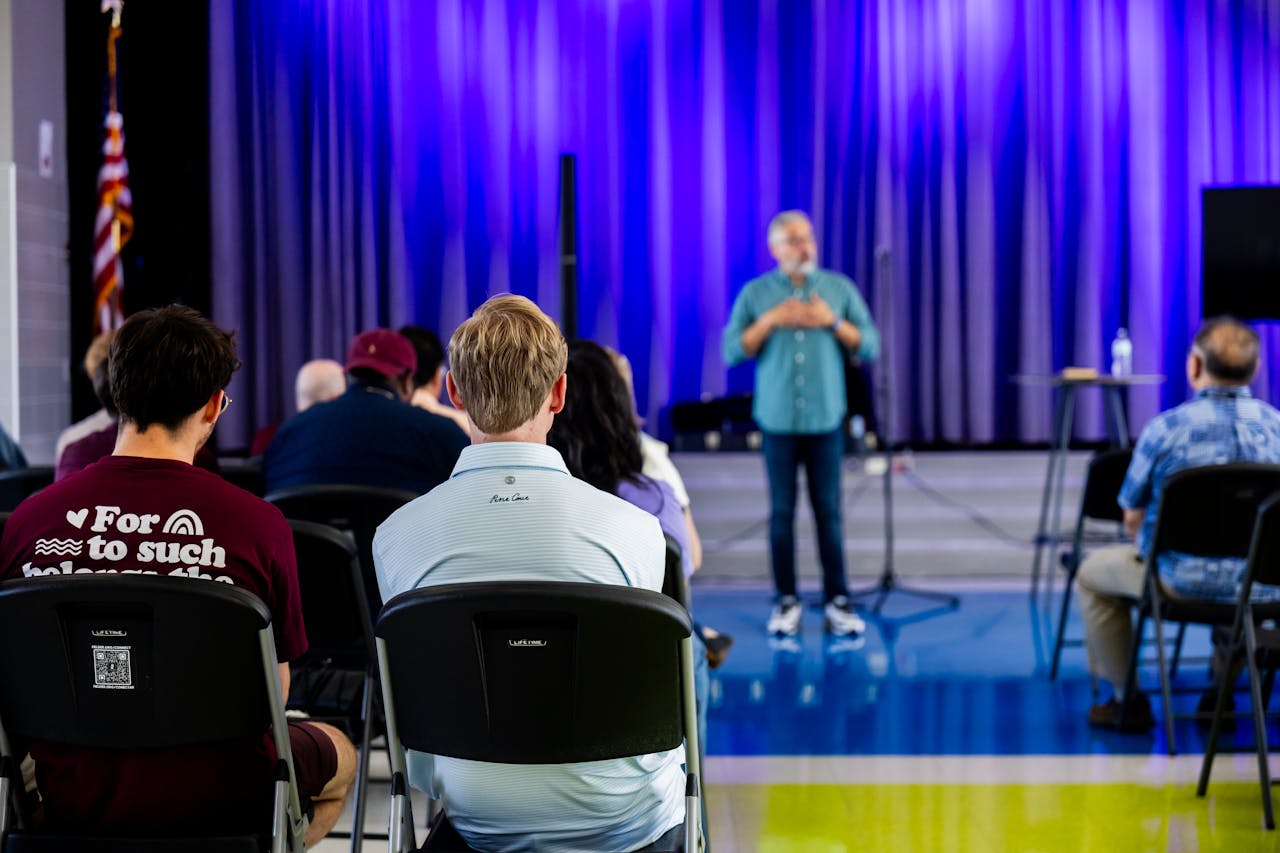 People listening to a speaker in a hall with blue lighting, exhibiting interest and engagement.