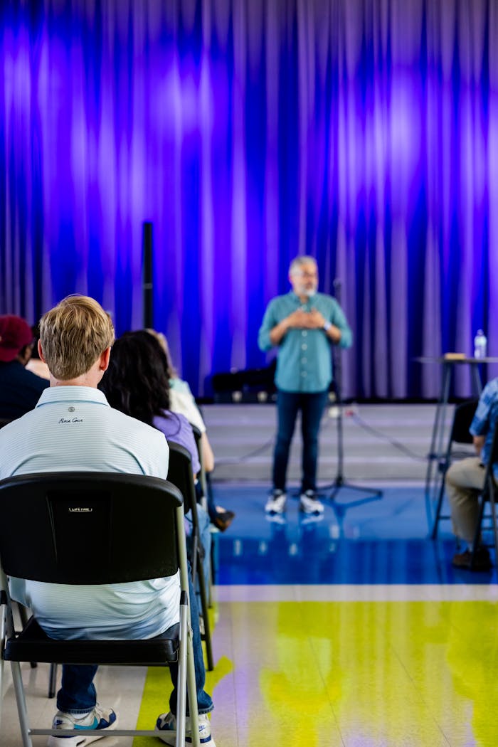 A speaker addressing a seated audience in a contemporary conference setting with a vibrant backdrop.